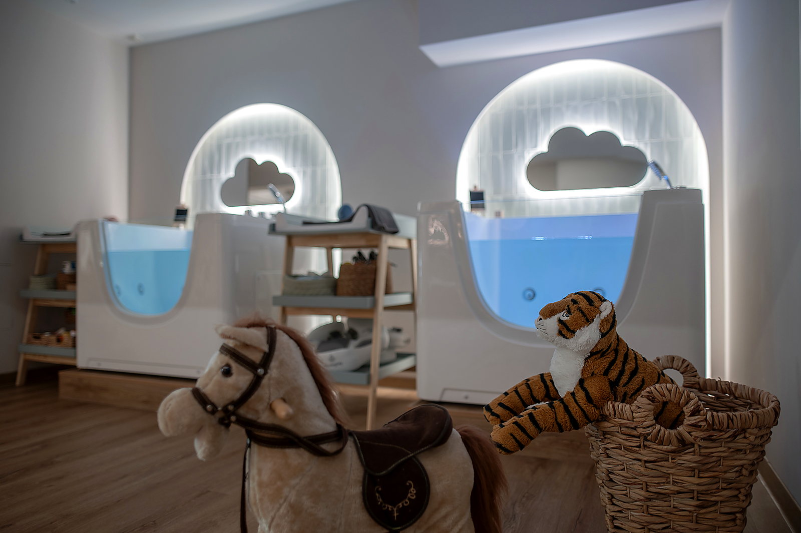 Οι δύο μπανιέρες του Baby Spa μπροστά σε φωτισμένες καμάρες, με ξύλινο αλογάκι και λούτρινα